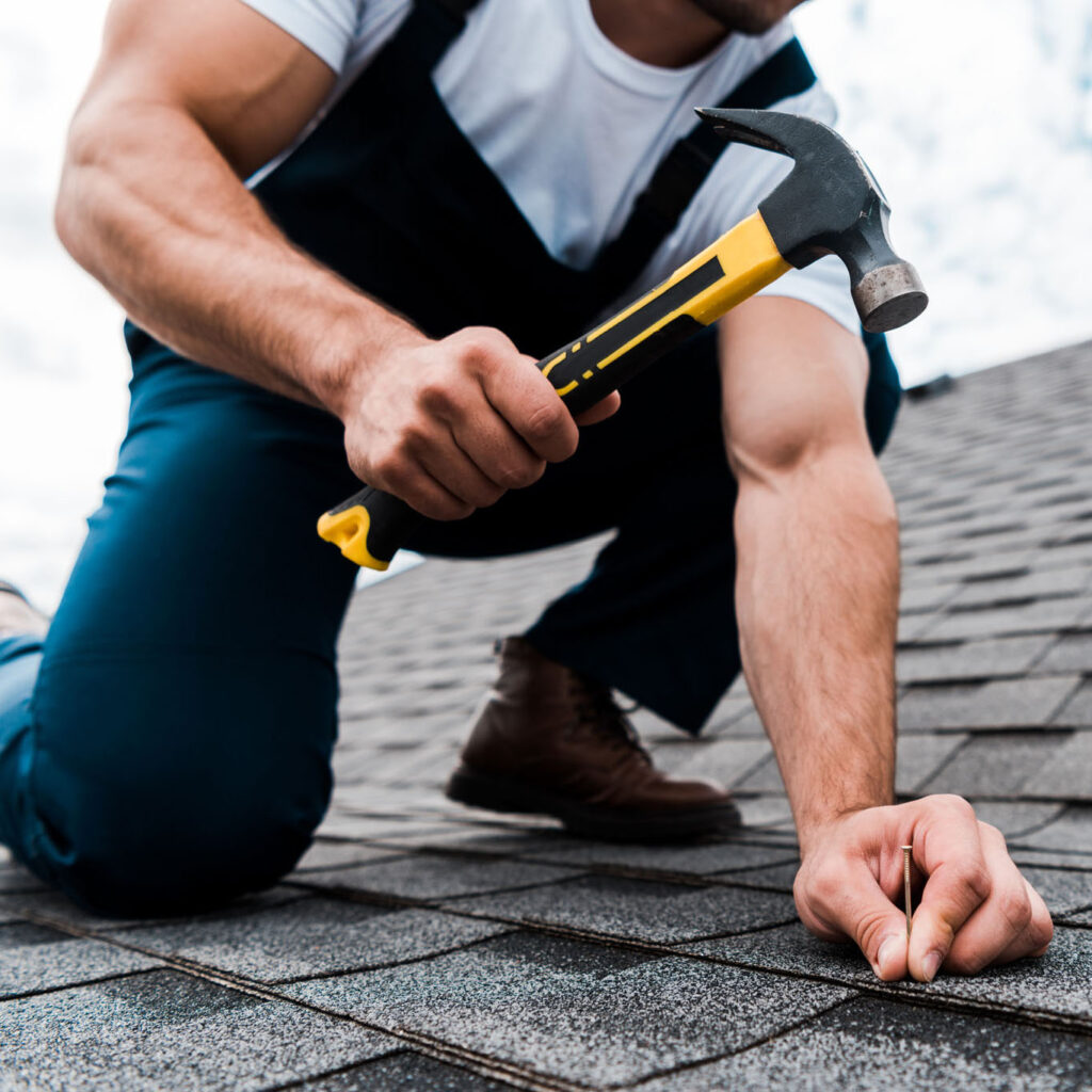 cropped view of handyman in uniform holding hammer while repairi Roofer working on a roof repair